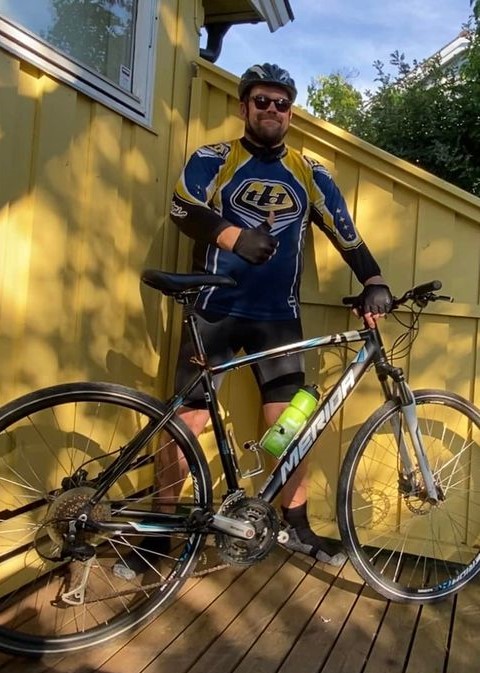 Mann i sykkelklær som står bak en sykkel av merket Merida og viser tommel opp.